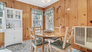 A wooden-paneled room with a round table, chairs, a cabinet, and a radiator. - Oak Nesting (Big Bear Lake)