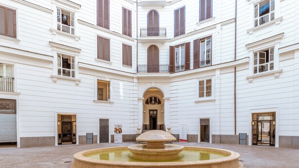 A courtyard with a central fountain, surrounded by white buildings with multiple windows and balconies. - Nana Inn Palazzo Nana' (Naples)