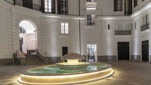A spacious courtyard with a central fountain, a staircase leading to an upper level, and a large arched doorway. - Nana Inn Palazzo Nana' (Naples)