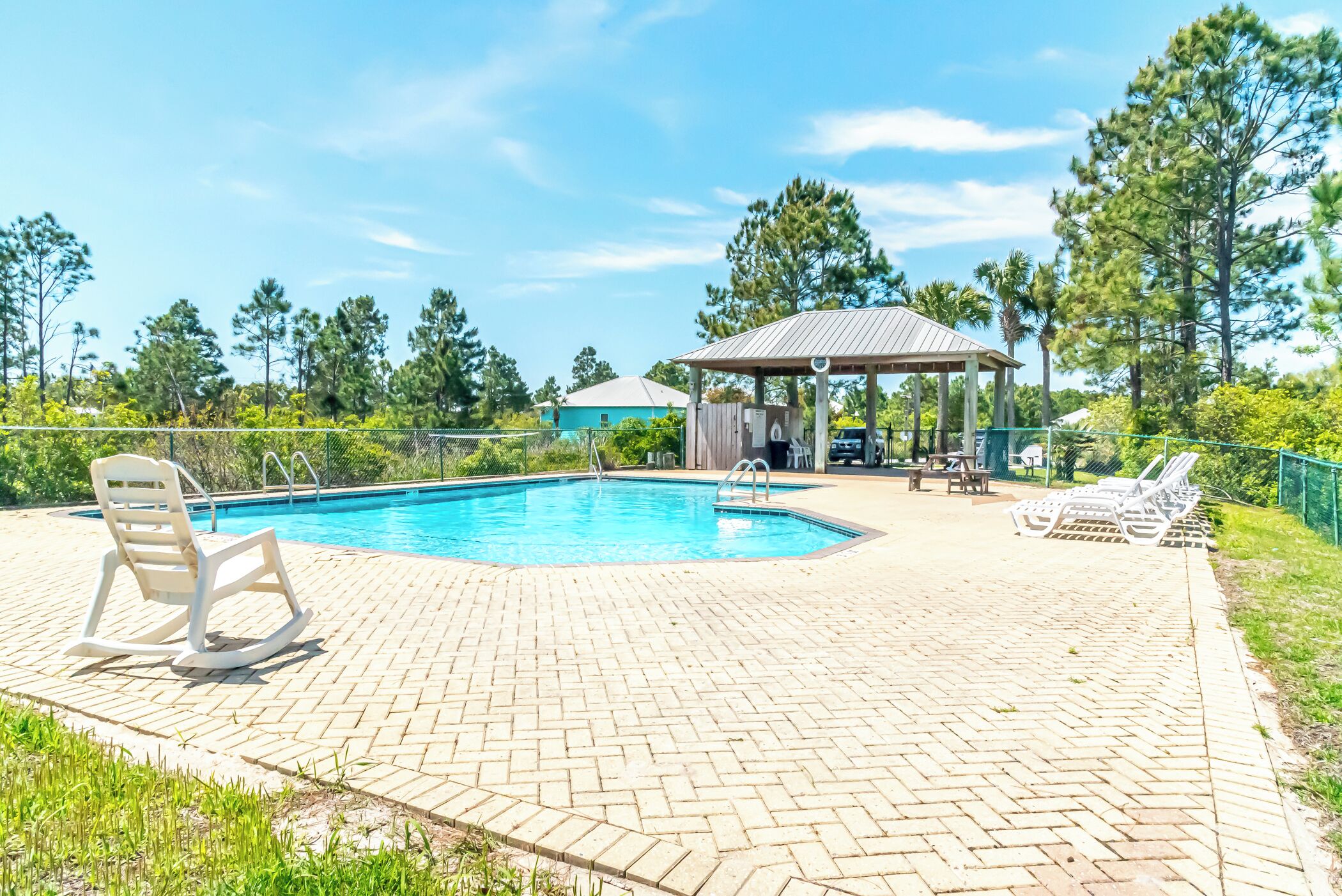A swimming pool with a gazebo, lounge chairs, and a brick patio.