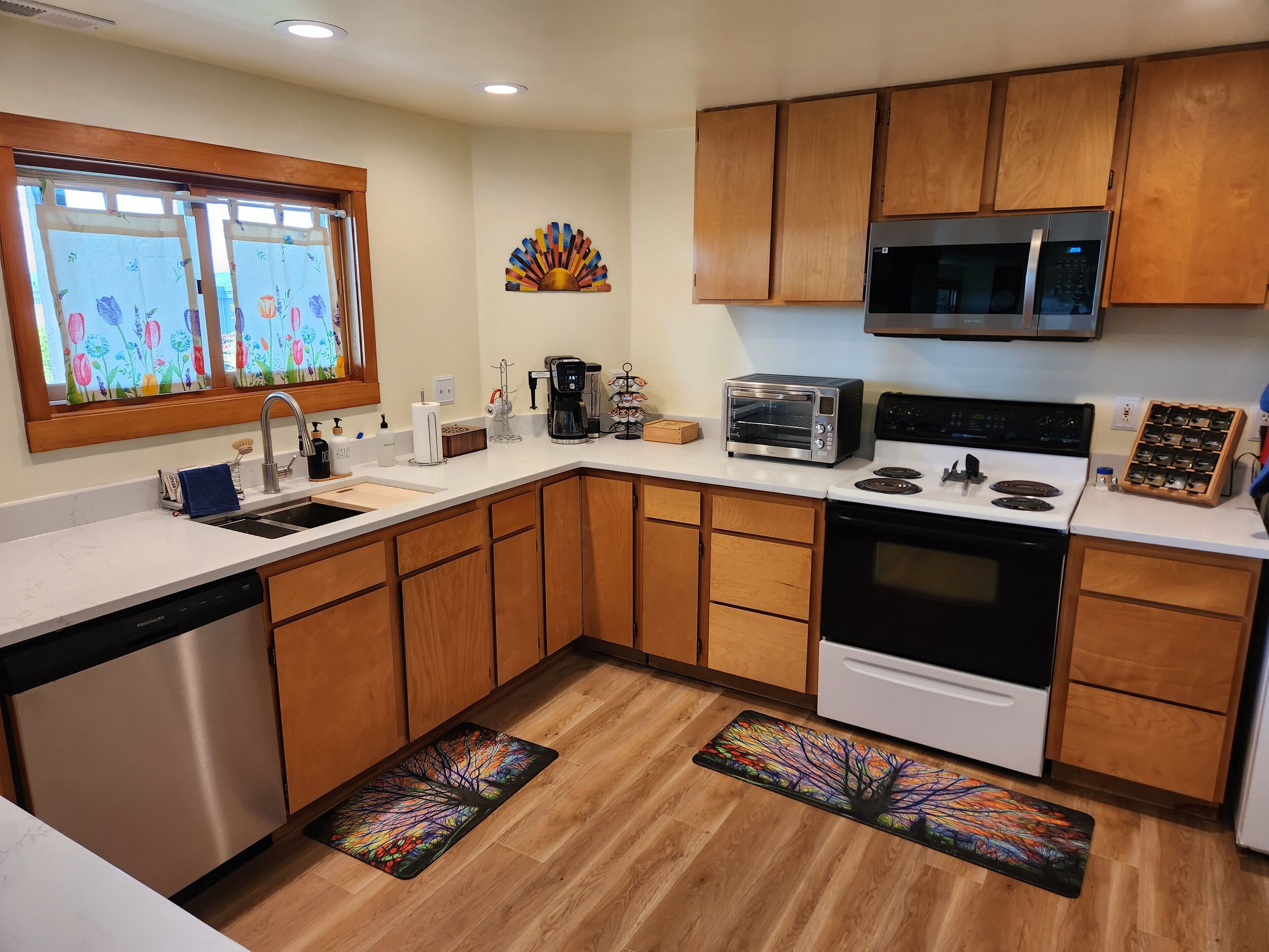 A modern kitchen with wooden cabinets, a stainless steel dishwasher, a microwave, a toaster oven, and a stove.