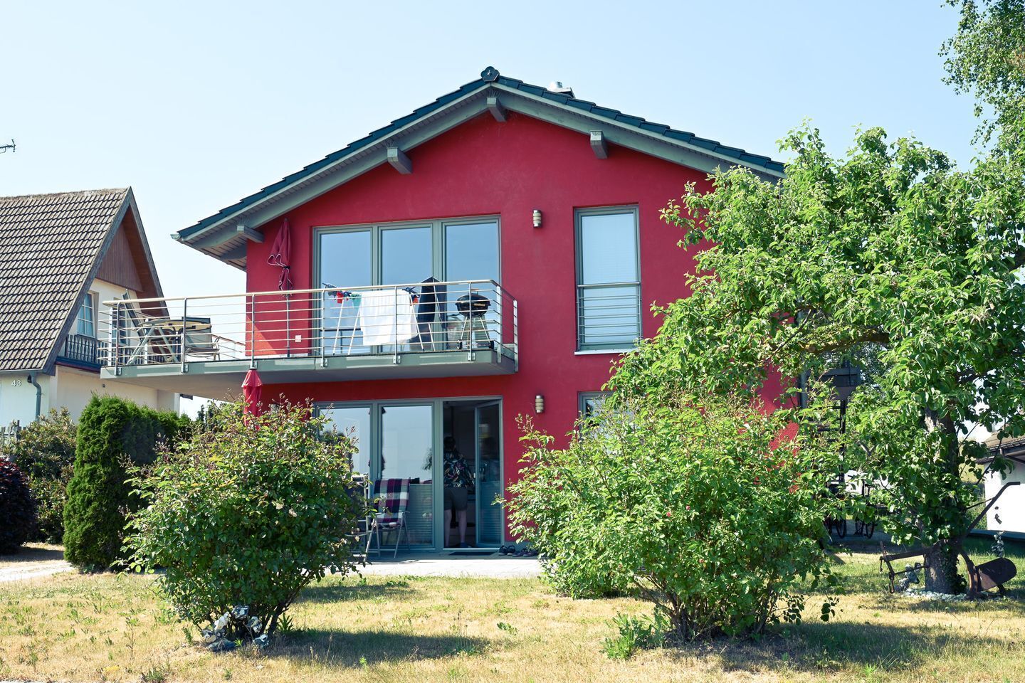 Uma casa de dois andares com fachada vermelha, uma varanda com grade e uma porta de entrada.