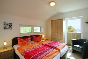 A bedroom with a bed, two bedside tables, a chair, a wardrobe, and a window with a view. - Haus Boddenblick Ferienwohnung OG - Ferienhaus Boddenblick - Fewo DG (Putbus)