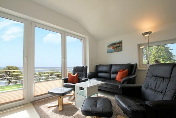 A modern living room with a glass coffee table, black leather sofas, and a view of the sea through large windows. - Haus Boddenblick Ferienwohnung OG - Ferienhaus Boddenblick - Fewo DG (Putbus)