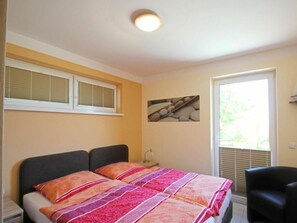 A bedroom with a bed, two bedside tables, a chair, a window with blinds, and a wall-mounted picture.