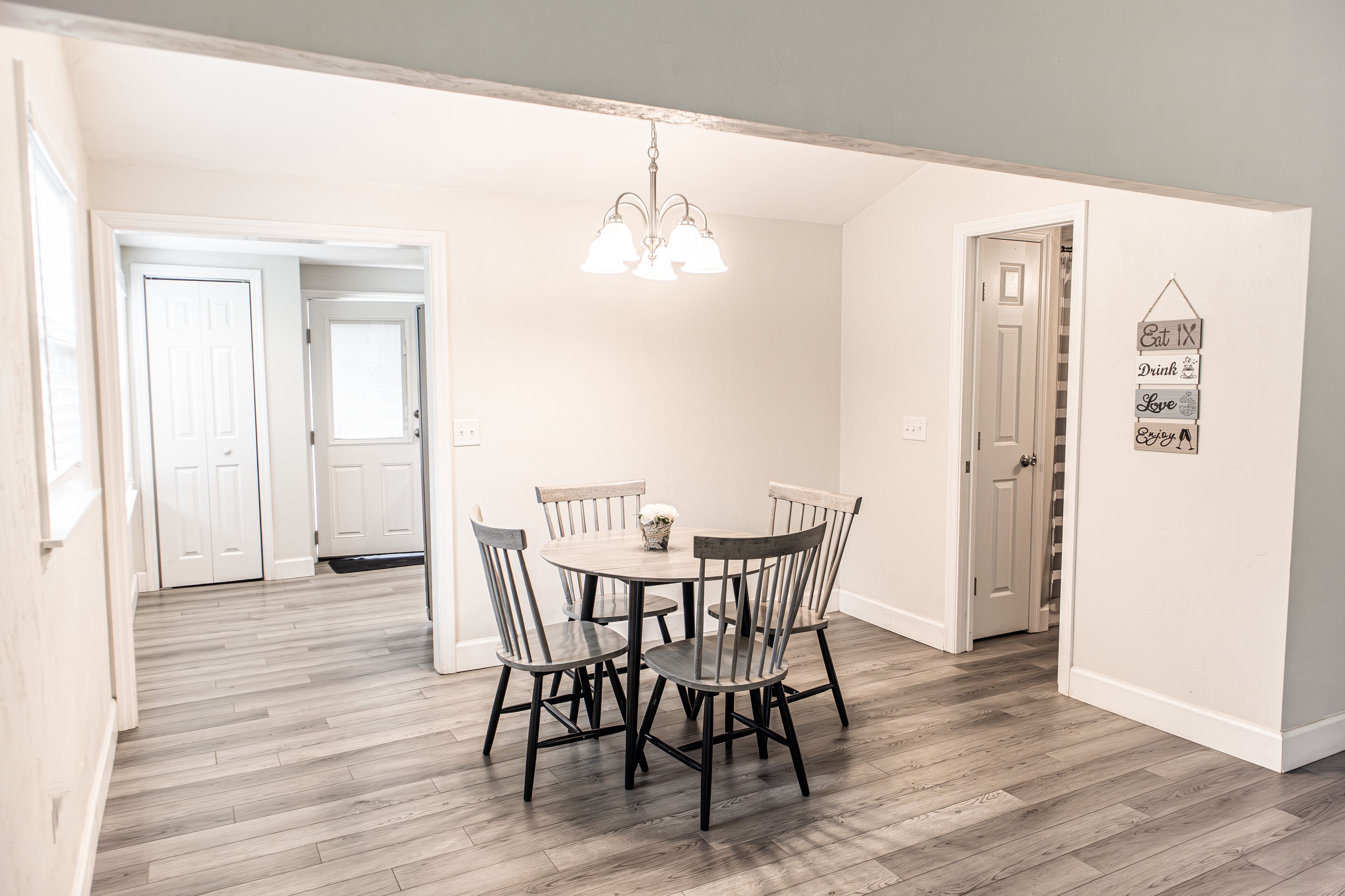 A dining area with a round table and four chairs, a chandelier, and a wall-mounted sign with motivational phrases.