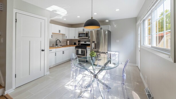 Una cocina moderna con armarios blancos, electrodomésticos de acero inoxidable y una mesa de comedor de vidrio.