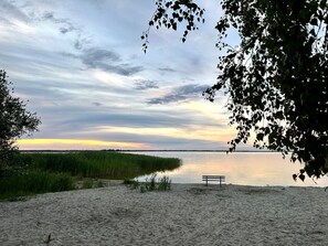 A bench on a sandy beach with a calm body of water and a cloudy sky.