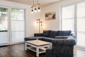 A modern living room with a grey sofa, a white coffee table, and a patterned armchair. There are two pendant lights hanging from the ceiling and a framed picture on the wall.