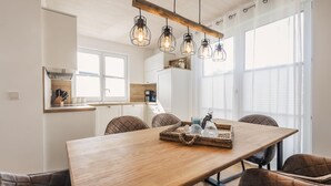Une cuisine moderne avec des meubles blancs, une table à manger en bois et des luminaires suspendus.