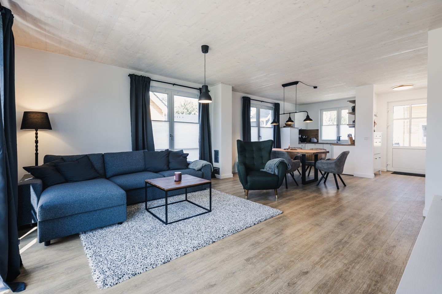 A modern living room with a sofa, coffee table, and a dining area with chairs and a table.