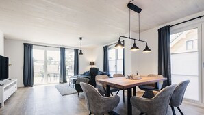 Un vaste espace de vie comprenant une table à manger en bois, des chaises à revêtement gris et un éclairage suspendu.