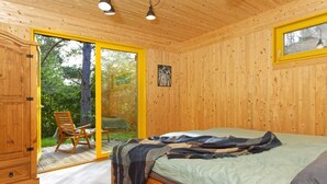 A wooden cabin bedroom with a bed, a chair, and a sliding door leading to a balcony.
