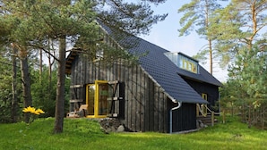 A rustic wooden cabin with a sloped roof, a front porch, and a stone foundation.