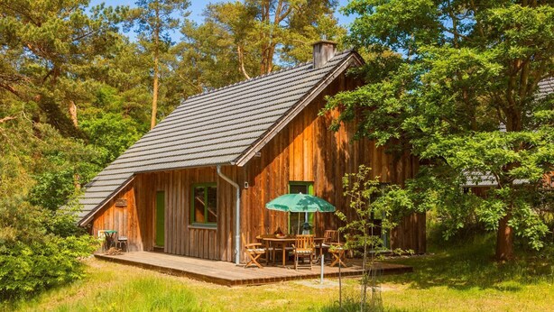 Une cabane rustique avec un toit en pente, un revêtement extérieur en bois et un petit porche doté de sièges pour l’extérieur.
