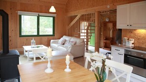 L’intérieur d’un chalet chaleureux, avec une table à manger en bois, deux bougies, un canapé blanc, un escalier et un coin cuisine.