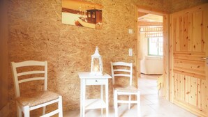 Une pièce avec un mur en bois, une table blanche surmontée d’une lanterne, deux chaises blanches et une porte en bois.