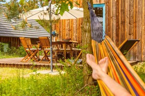 A wooden deck with outdoor furniture, a hammock, and a rustic building in the background. - Exklusives, 65 qm Großes Ferienhaus für 5 Personen. - Minna-busch-weg (Loddin)