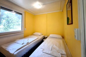 A room with two single beds, a window, and a wall-mounted light fixture.