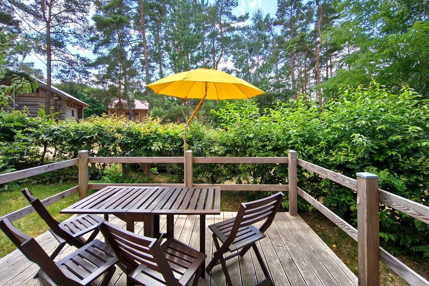 Une terrasse en bois avec une table et des chaises, entourée d’une clôture en bois et d’une végétation luxuriante.