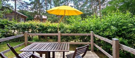 A wooden deck with a table and chairs, surrounded by a wooden fence and lush greenery.
