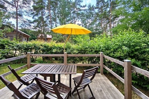 Une terrasse en bois avec une table et des chaises, entourée d’une clôture en bois et d’une végétation luxuriante.
