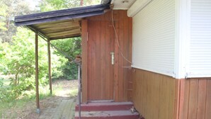 A wooden house with a covered porch and a closed garage door. - Gemütliches, 30 qm Großes Ferienhaus für 4 Personen. - Minna-busch-weg (Loddin)