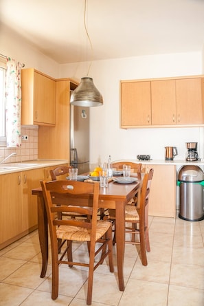 A kitchen with wooden cabinets, a dining table with chairs, a hanging light fixture, and a coffee maker.