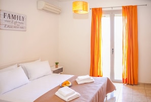A bedroom with a bed, pillows, a bedside table with a plant, a sign on the wall, and orange curtains.
