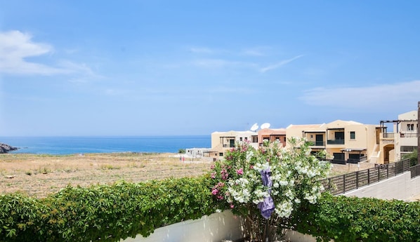 A coastal hotel with multiple buildings, a view of the sea, and a garden with flowering plants.