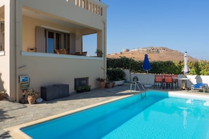 A swimming pool with a view of a hill, outdoor furniture, and potted plants.