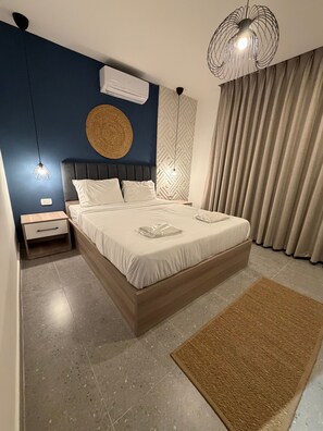 A modern bedroom with a large bed, a bedside table, an air conditioning unit, a decorative wall hanging, and a textured rug. - JRE Abdoun Rooftop 2bedroom Kh&sh 02 (Amman)