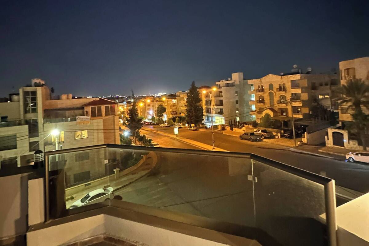 A nighttime cityscape with buildings, a street, and a pedestrian walkway.