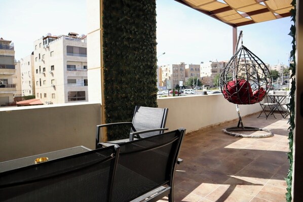 A balcony with a hanging chair, a table, and chairs.