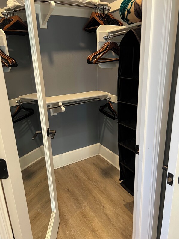 A walk-in closet with wooden flooring, a white door, and a grey wall.