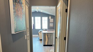A hallway with a kitchen area in the background, featuring a white countertop and a stainless steel refrigerator.