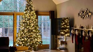 A living room with a large Christmas tree, a fireplace, and a view through a large window.