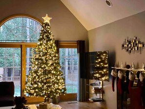 Ein Wohnzimmer mit einem großen Weihnachtsbaum, einem Kamin und Blick durch ein großes Fenster.