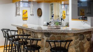 A kitchen with a stone island, bar stools, a wooden ceiling, and a TV mounted on the wall.
