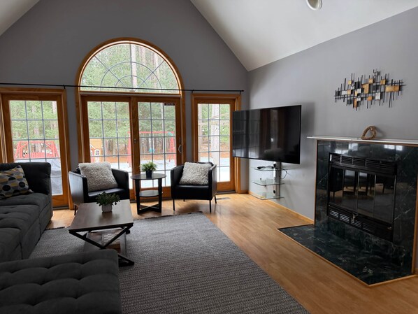 A modern living room with a fireplace, large windows, and a TV.