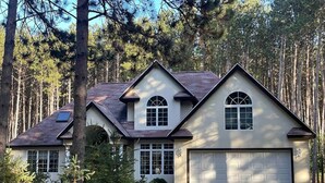 A two-story house with a garage, surrounded by tall pine trees.