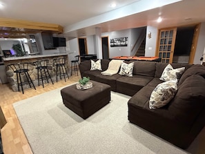 Un salon avec un canapé d’angle marron, une table basse et un coin bar équipé de tabourets.