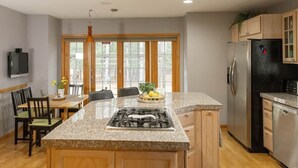 A kitchen with a central island, wooden cabinets, a refrigerator, and a dining area with chairs.