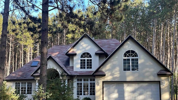 A two-story house with a garage, surrounded by tall pine trees.