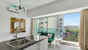 A modern kitchen with a large window, a green sofa, and a view of the city. - Central Suites Tower (Santo Domingo)