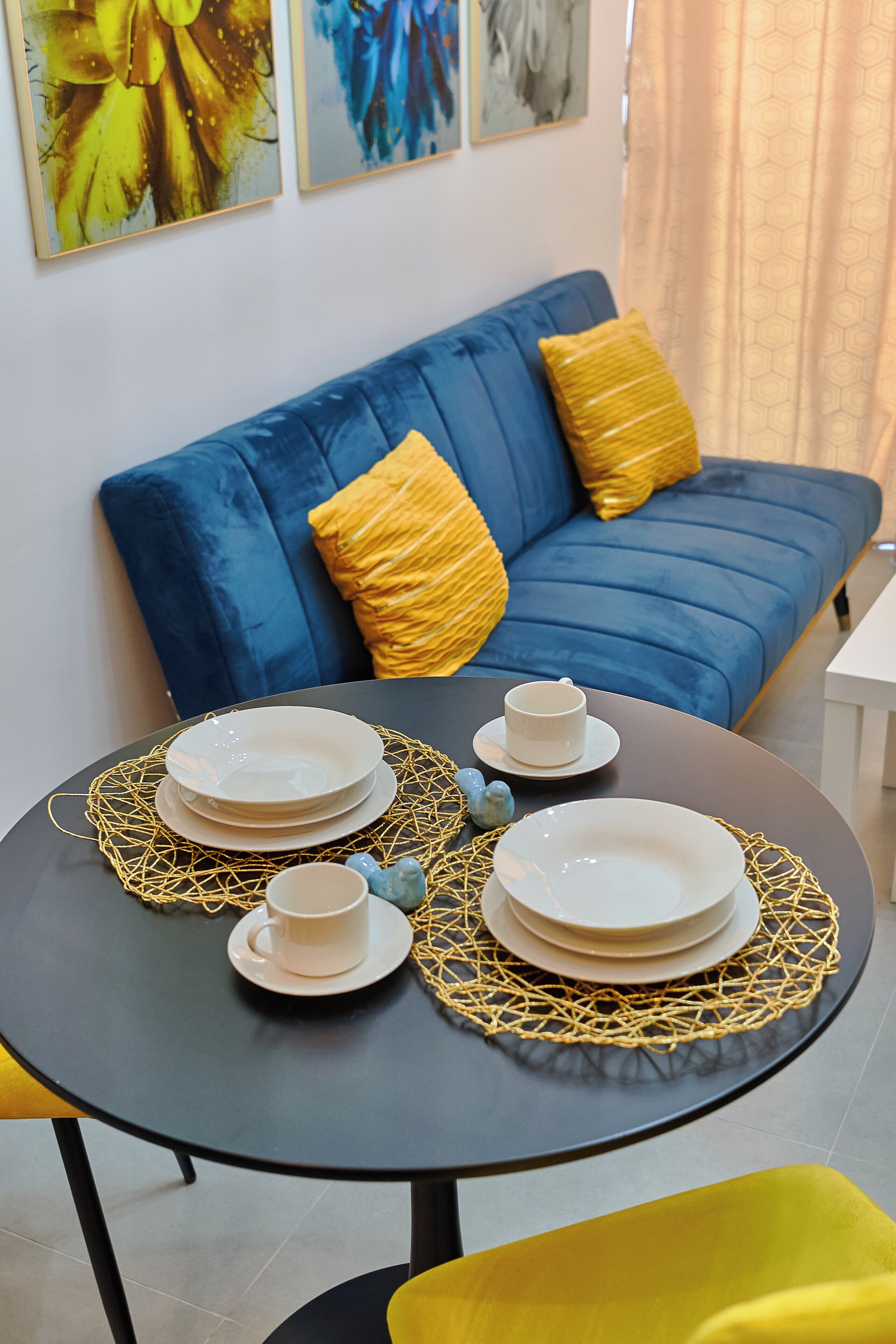 A dining table with plates, cups, and a decorative net. A blue sofa with yellow cushions is in the background.