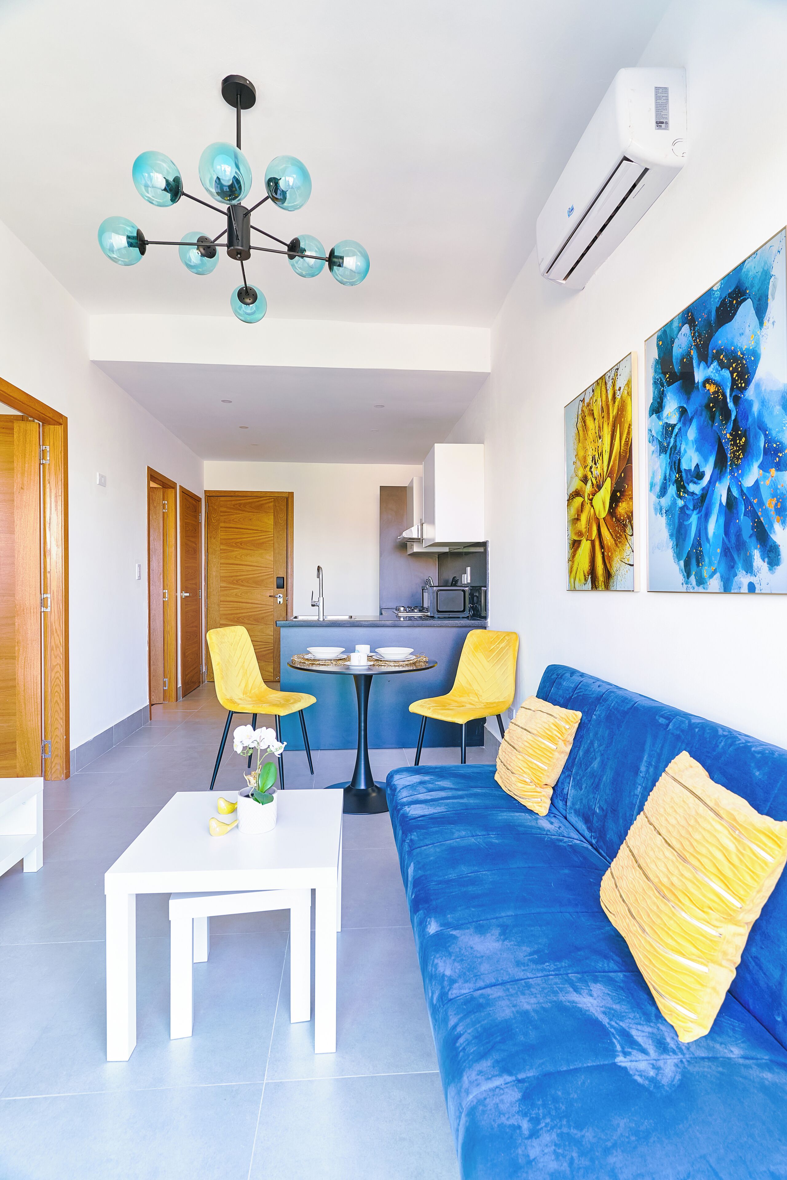 A modern living room with a blue sofa, yellow chairs, a white coffee table, and a chandelier.