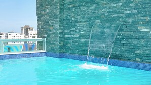 A swimming pool with a water feature, a tiled border, and a stone wall. - Central Suites Tower (Santo Domingo)
