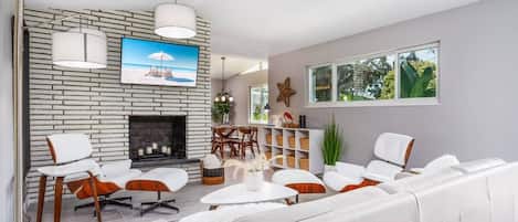 A modern living room with a fireplace, white sofas, and a television mounted on a brick wall.