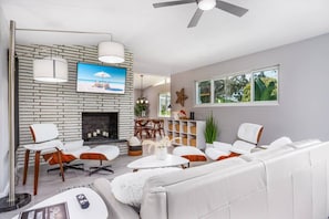 A modern living room with a fireplace, white sofas, and a television mounted on a brick wall.